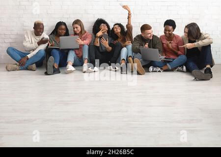 Gruppo internazionale di Millennial che si agghiacciano insieme, utilizzando gadget Foto Stock