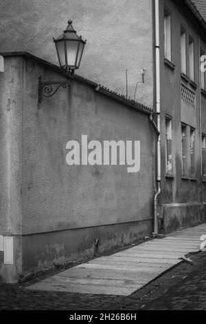 foto in bianco e nero di una strada che ha bisogno di essere ristrutturata con marciapiede danneggiato e facciate con una vecchia lampada da strada dilapidata Foto Stock