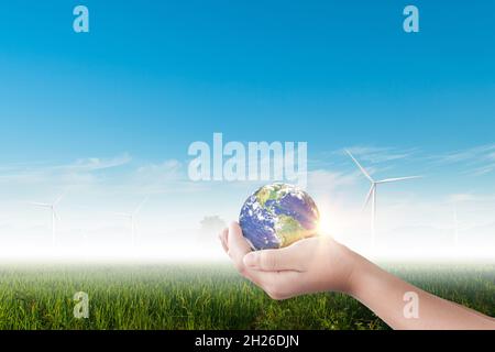 Mani che tengono terra, globo su campo di turbina eolica su sfondo cielo blu. Concetto di ambiente Foto Stock