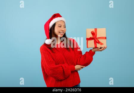 Festa invernale. Felice signora asiatica in Babbo Natale cappello scatola con regalo per Capodanno o Natale Foto Stock