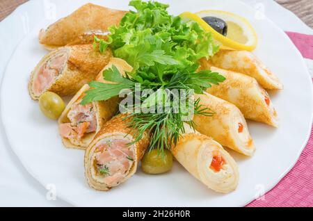 Pancake ripieni di pesce, formaggio e caviale rosso guarniti con erbe su un piatto bianco da vicino Foto Stock