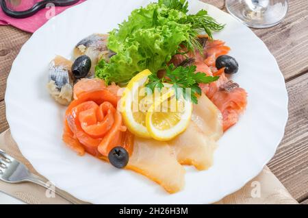 Filetto di diversi tipi di pesce - rosso, aringa con limone e lattuga su un piatto bianco primo piano Foto Stock