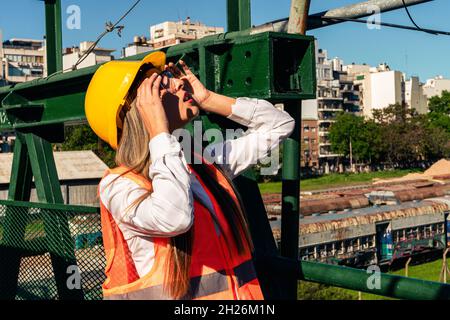 Bella giovane ingegnere femminile o supervisore, indossando attrezzature di sicurezza, ispeziona un ponte pedonale ferroviario. Concetto di donna emancipata, professione Foto Stock