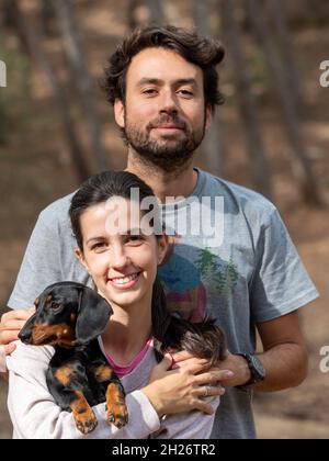 Felice giovane coppia caucasica sorridente con il loro cane in miniatura Dachshund nella foresta durante l'autunno Foto Stock