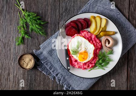 labskaus, carne di manzo, purè di patate con barbabietole ricoperte di uova fritte, barbabietole affettate, sottaceti e aringhe arrotolate su un piatto, cui tedesco Foto Stock