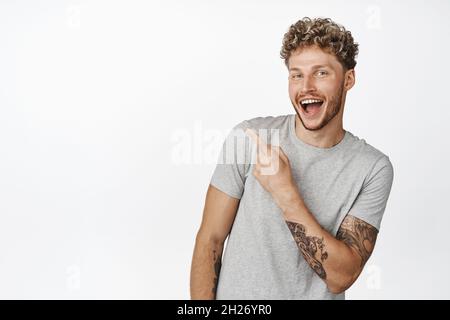 Allegro attraente giovane uomo puntando dito in alto a sinistra angolo, ridendo e sorridendo, clienti intivint check out negozio, mostrando pubblicità Foto Stock
