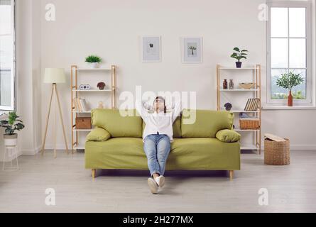 Felice uomo giovane rilassato seduto su un comodo divano nel soggiorno del suo appartamento Foto Stock