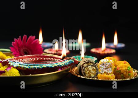 Grande Clay Diya illuminato con indiano Mithai Laddu, Meetha Laddoo, Burfi, Anjeer Roll, Red Flower e Small dia. Tema per Diwali Pooja, Navratri, Dusseh Foto Stock