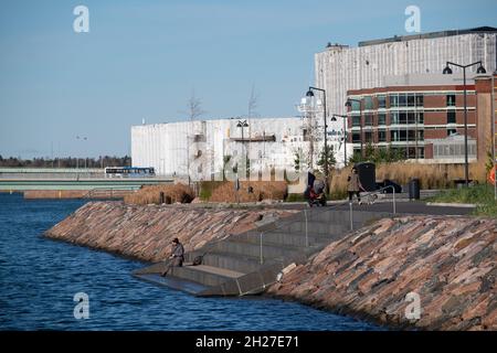 Helsinki / Finlandia - 19 OTTOBRE 2021: Un uomo da solo che pesca sulla riva del distretto residenziale di Ruoholahti. Foto Stock