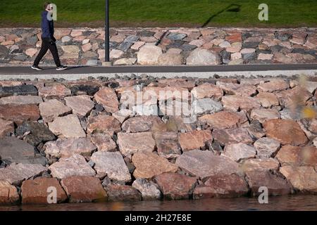 Helsinki / Finlandia - 19 OTTOBRE 2021: Un uomo da solo che cammina nel parco pubblico sulla riva del quartiere residenziale di Ruoholahti Foto Stock