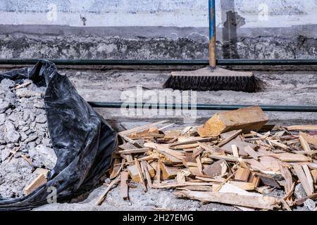 Rifiuti di costruzione detriti in busta di plastica nera e su vecchio pavimento di cemento, da sala demolita, spazzatura sfocata sullo sfondo, vista ravvicinata Foto Stock