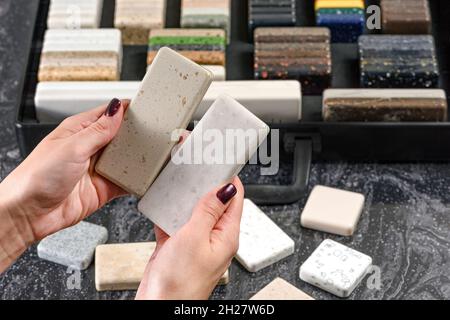 Campioni di materiale per il piano di lavoro. Le mani femminili stanno scegliendo gli elementi interni per la ristrutturazione. Campioni di pietra acrilica in mani. Foto Stock