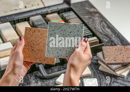 Campioni di materiale per il piano di lavoro. Le mani femminili stanno scegliendo gli elementi interni per la ristrutturazione. Campioni di pietra acrilica in mani. Foto Stock