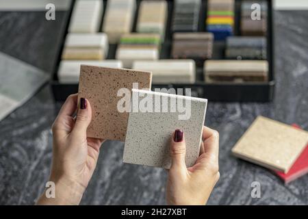 Campioni di materiale per il piano di lavoro. Le mani femminili stanno scegliendo gli elementi interni per la ristrutturazione. Campioni di pietra acrilica in mani. Foto Stock