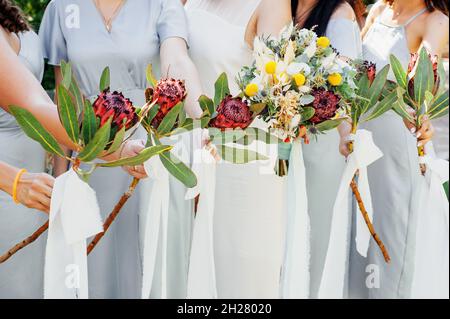 Bridesmaids in abiti blu e sposa con bei mazzi di fiori protea. Bellissimo matrimonio di lusso blog concetto. Matrimonio estivo. Foto Stock