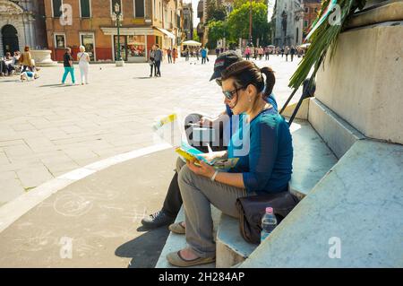 VENEZIA, ITALIA - Apr 30, 2016: I turisti non identificati seduti da una statua che legge una mappa nel centro della città Foto Stock