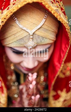 Primo piano del ritratto facciale di donna asiatica che indossa il vestito tradizionale Minangkabau inchinandosi con le mani messe insieme nella cerimonia nuziale. Espressione felice. Foto Stock