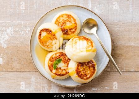 Syrniki, frittelle di formaggio cottage con miele su piatto, isolato su tavola di legno vista dall'alto Foto Stock