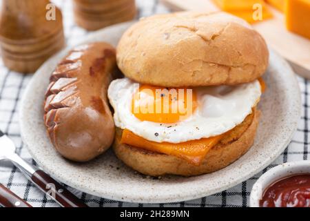 Sandwich all'americana con salsiccia, uova e formaggio sul piatto, vista sul primo piano. Cibo per la colazione malsano Foto Stock