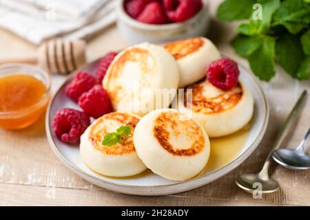 Frittelle di formaggio, pancake o sciroppi con miele su un tavolo di legno servito con lamponi freschi, vista sul primo piano Foto Stock