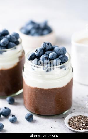 Budino di semi di chia al cioccolato con yogurt e mirtilli in un vaso. Snack vegetariano sano Foto Stock