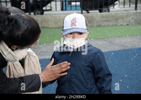 Istruzione Preschool 3-4 anni insegnante attento che si appoggia sopra per vedere come il ragazzo si sente, sul parco giochi, maschere per il viso per proteggere da Covid-19 Foto Stock