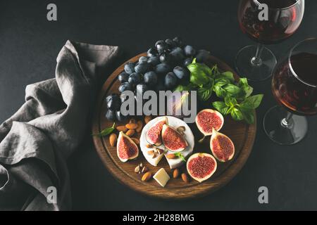 Formaggio bianco brie o camembert con fichi e uva su tavola di legno, servito con un bicchiere di vino. Immagine in tonalità della vista dall'alto. Set di antipasti a base di formaggio e vino Foto Stock