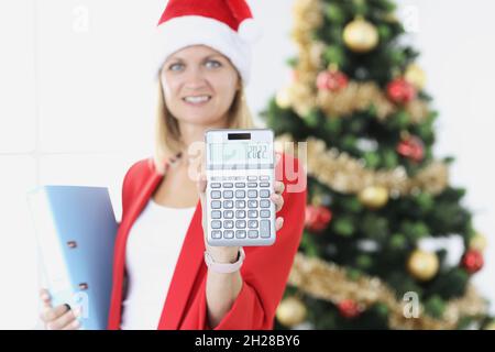 Businesswoman sta tenendo calcolatrice con i numeri 2022 sullo sfondo di albero di Capodanno Foto Stock