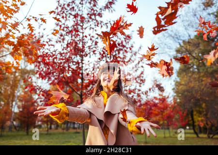 Attività della stagione autunnale. Donna lancio foglie in autunno parco. Giovane donna che si diverte tra gli alberi rossi all'aperto Foto Stock
