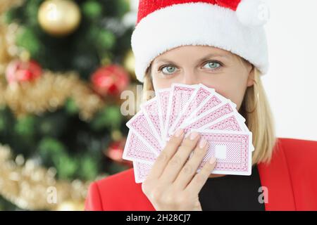 Ritratto di giovane bella donna in babbo natale cappello tenendo carte da gioco sullo sfondo di albero di Capodanno Foto Stock