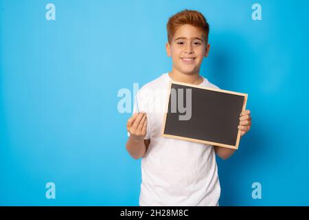 Il ragazzo dai capelli rossi tiene il cartellone vuoto isolato su sfondo blu. Foto Stock