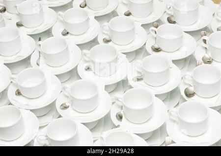 Un sacco di tazze per caffè o tè su un tavolo con cucchiai e zucchero Foto Stock