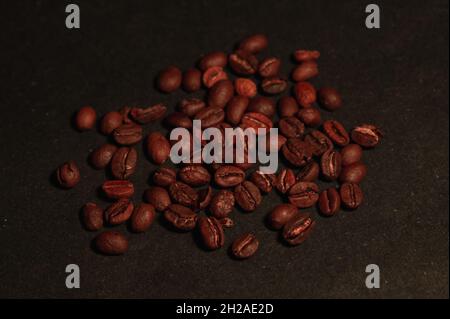 i chicchi di caffè arrosto sono sparsi casualmente su uno sfondo nero sotto una luce blu su una superficie piana Foto Stock