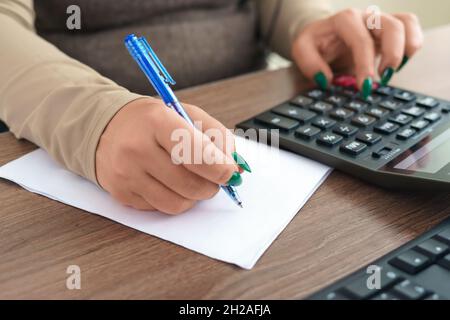 Analisi dei dati finanziari. Primo piano di una mano di una donna d'affari che scrive e conta sulla calcolatrice in ufficio. Messa a fuoco selettiva Foto Stock