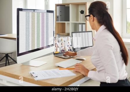 Donna che usa più computer da ufficio, lavora con fogli di calcolo e fa una videochiamata Foto Stock