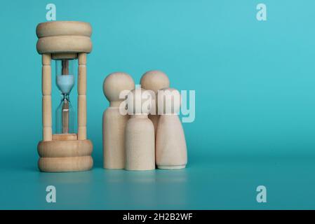 Tempo di qualità con concetto di famiglia. Bambole in legno e clessidra su sfondo verde con spazio copia Foto Stock