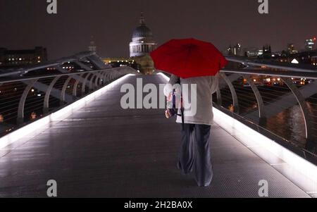 RITRASMESSO CORRETTORE DATA A WDNESDAY OTTOBRE 20 Una donna cammina attraverso il Millennium Bridge a Londra mercoledì sera. I servizi di emergenza hanno ricevuto un elevato numero di chiamate da parte di persone che hanno segnalato inondazioni dopo che l'Inghilterra meridionale è stata colpita da una notte da forti piogge e venti forti da una tempesta che si è spostata dalla Francia. Data foto: Mercoledì 20 ottobre 2021. Foto Stock