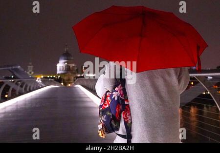 RITRASMESSO CORRETTORE DATA A WDNESDAY OTTOBRE 20 Una donna cammina attraverso il Millennium Bridge a Londra mercoledì sera. I servizi di emergenza hanno ricevuto un elevato numero di chiamate da parte di persone che hanno segnalato inondazioni dopo che l'Inghilterra meridionale è stata colpita da una notte da forti piogge e venti forti da una tempesta che si è spostata dalla Francia. Data foto: Mercoledì 20 ottobre 2021. Foto Stock