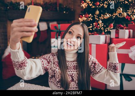 Foto di sognante divertente donna matura indossare stampa maglione sorridente registrazione vlog di natale in casa stanza casa Foto Stock