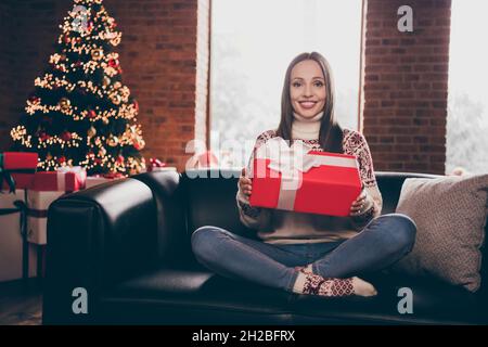 Foto full size di impressa cute mature lady sit sul divano tenere presente indossare jeans maglione calze nuovo anno a casa Foto Stock