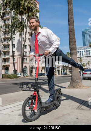 Ragazzo felice in formalwear ride stand-up e-scooter lungo il marciapiede, attivo Foto Stock