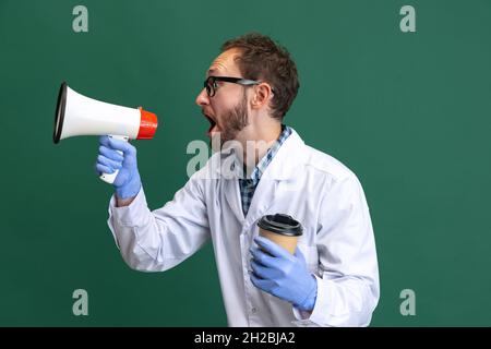 Ritratto di giovane uomo che indossa abito bianco e guanti protettivi che hanno divertimento isolato su sfondo verde. Foto Stock