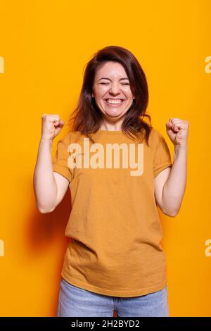 Ritratto di donna eccitata sorridente e aggrappante pugni davanti alla fotocamera. La persona allegra si sente molto gioiosa e mostra una pressione facciale positiva. Piacere adulto sensazione di eccitazione Foto Stock