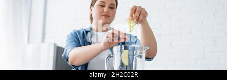 Donna sfocata con sovrappeso mettere fette di mela in frullatore in cucina, banner Foto Stock