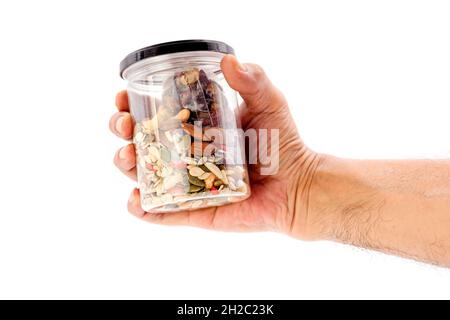 Mano umana che tiene grani interi e bottiglia di plastica di frutta secca isolata su sfondo bianco. Foto Stock