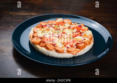 Pizza, salsiccia e bastoncini di granchio in un piatto di ceramica su un tavolo di legno. Foto Stock