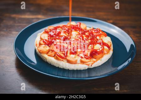 Mettere la salsa di pomodoro sulla pizza, la salsiccia e i bastoncini di granchio in un piatto di ceramica su un tavolo di legno. Foto Stock