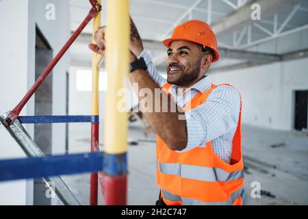 Giovane e bel costruttore che si arrampica su ponteggi in cantiere Foto Stock