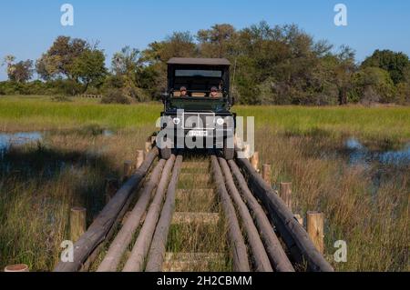 Un veicolo safari che attraversa un ponte di tronchi ad Abu Camp. Abu Camp, Delta Okavango, Botswana. Foto Stock