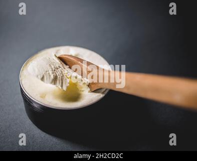 Corpo di burro con cucchiaio di legno su sfondo scuro. Cosmetici naturali e cura del corpo. Con spazio di copia. Foto Stock